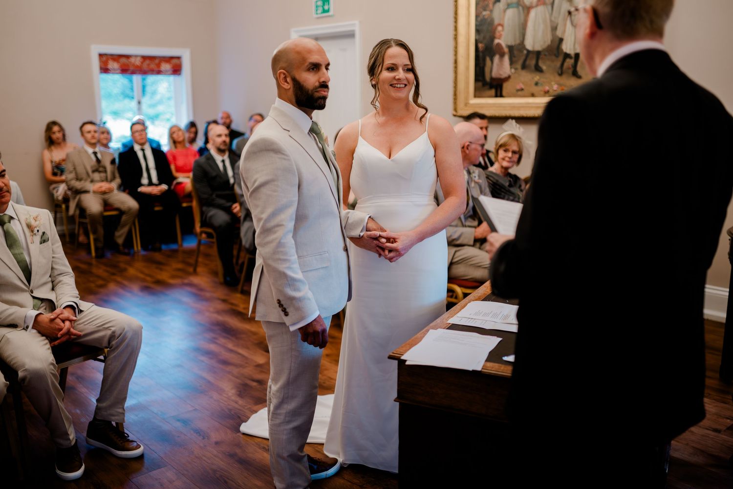 Bride and groom stand before officiant during intimate wedding ceremony with seated guests in elegant venue.