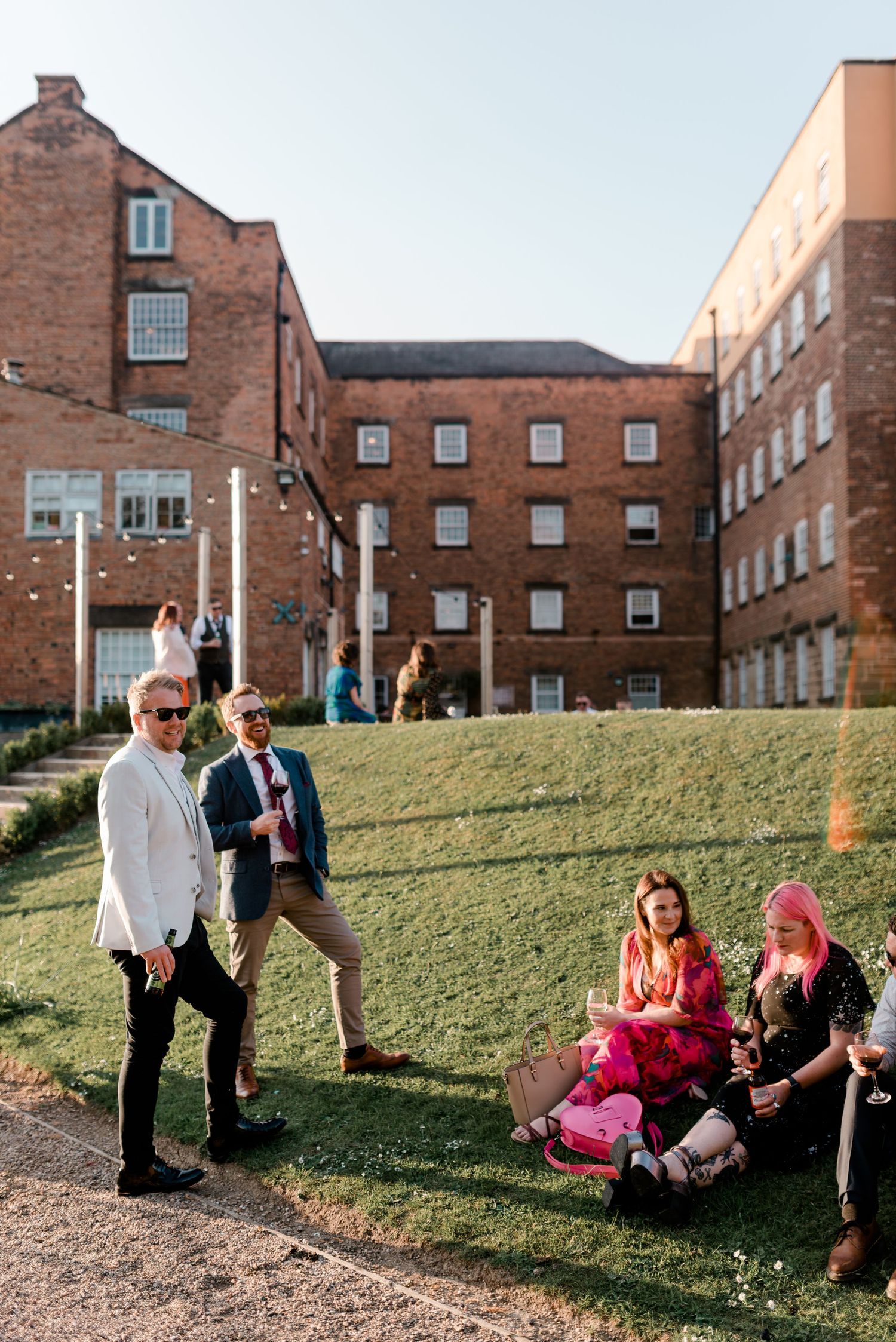 A group relaxes on a grassy hill outside a brick university building on a sunny day.