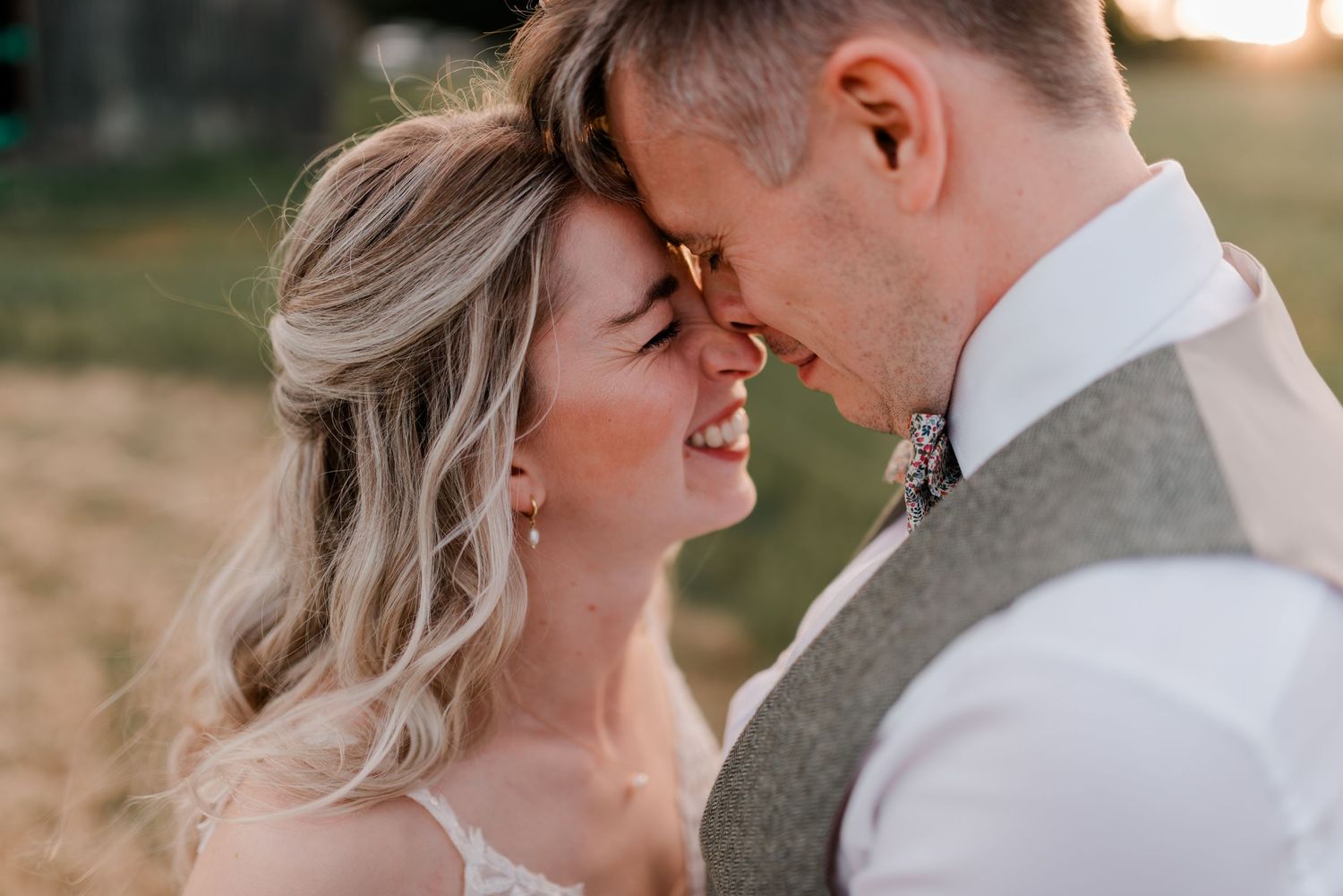 Bride and groom share a romantic forehead-to-forehead moment, smiling softly in warm golden sunset light.