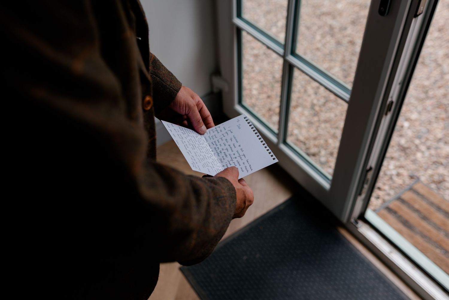 Groom reading handwritten wedding vows from a notepad by a window on his wedding day.