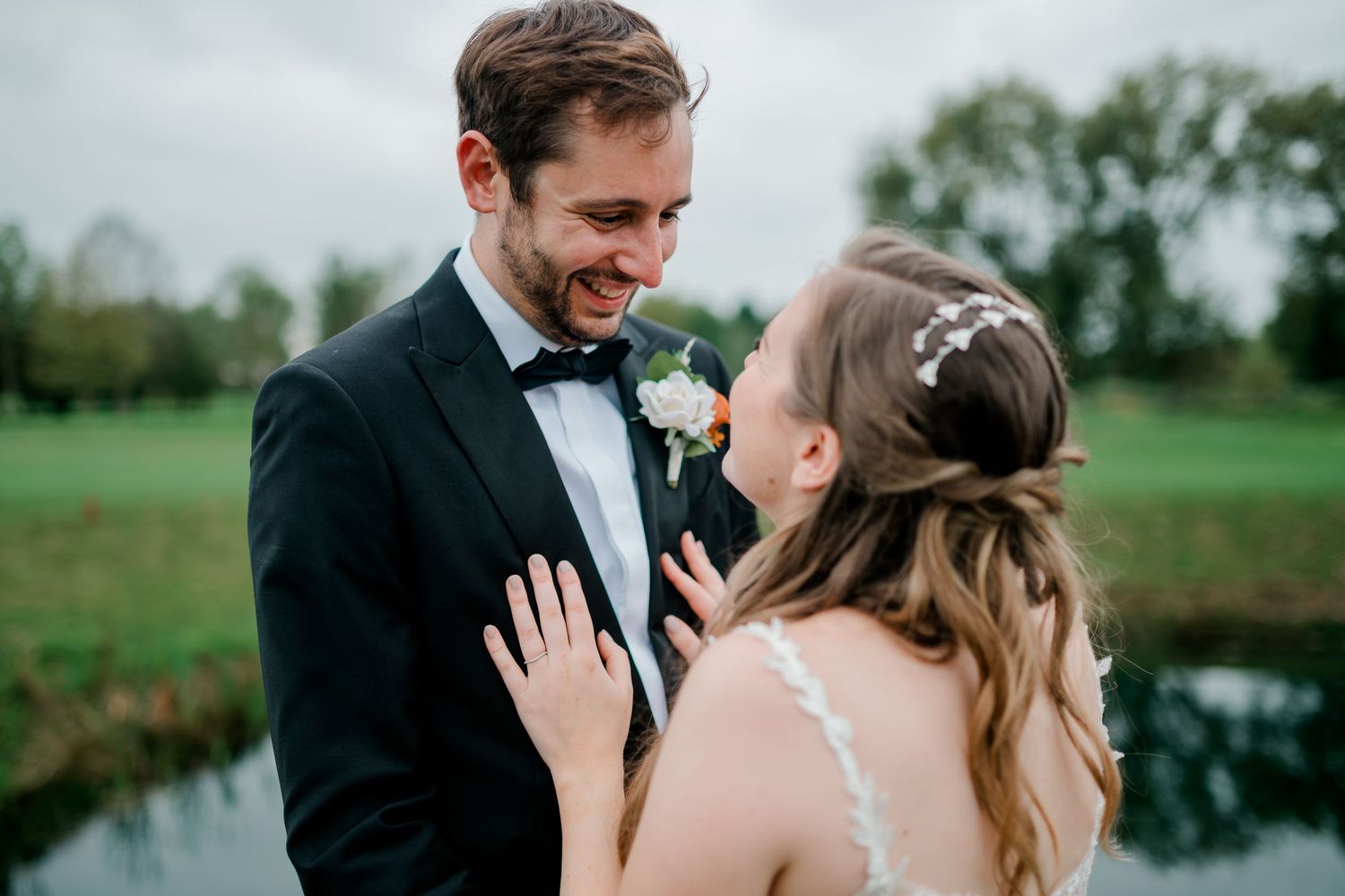 A happy couple shares intimate moments during their outdoor wedding photoshoot near a scenic pond.
