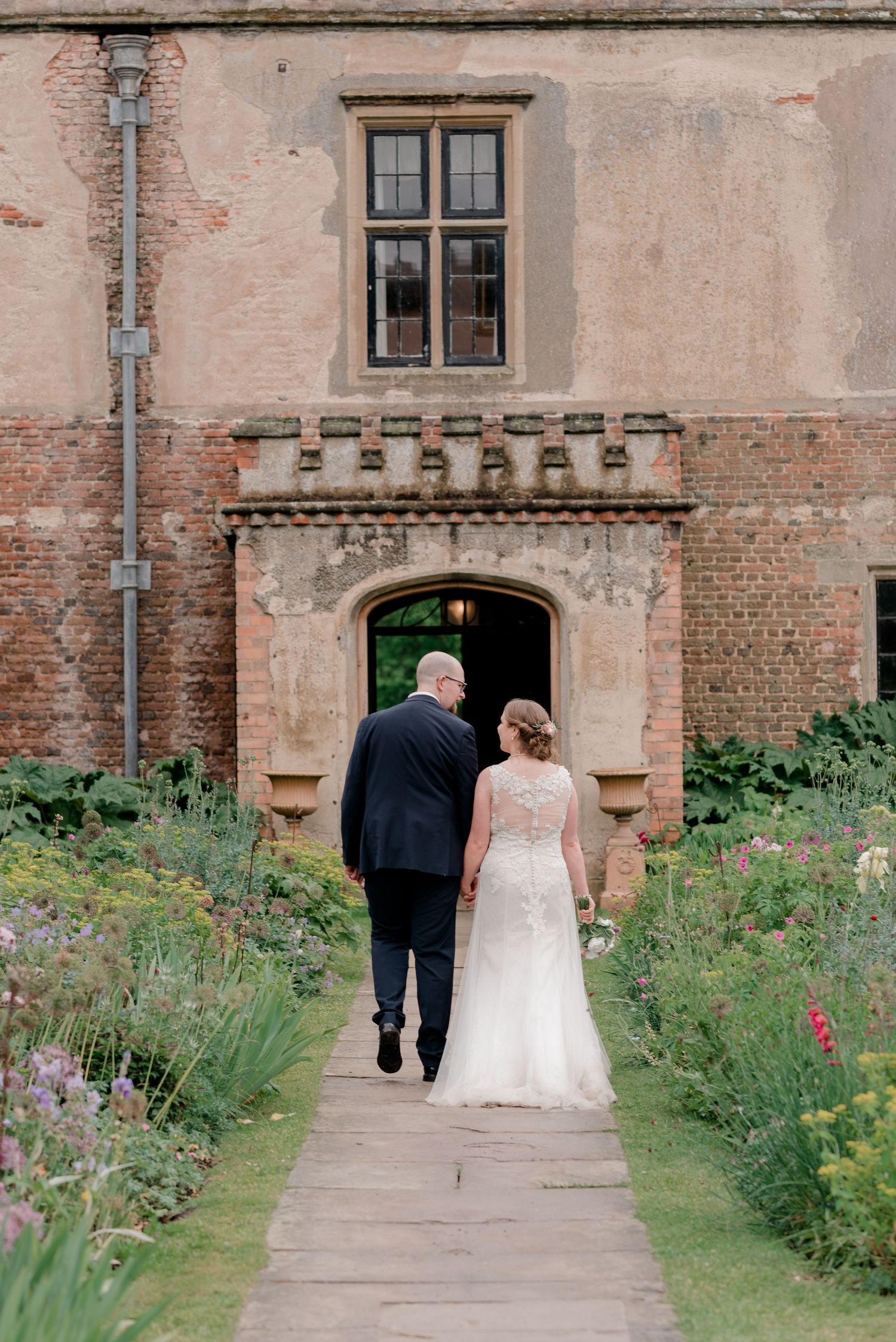 Couple walking down garden path towards historic building entrance.