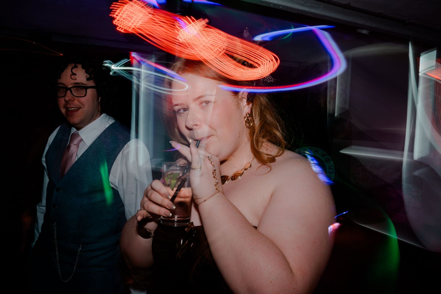 Wedding guest dancing under colorful neon light trails at a lively evening reception party.