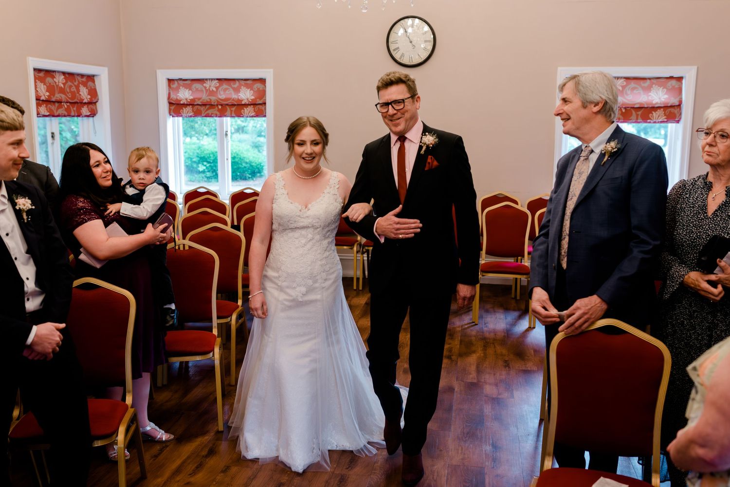 Bride and groom walk down the aisle smiling at a wedding ceremony in an elegant room with red chairs.