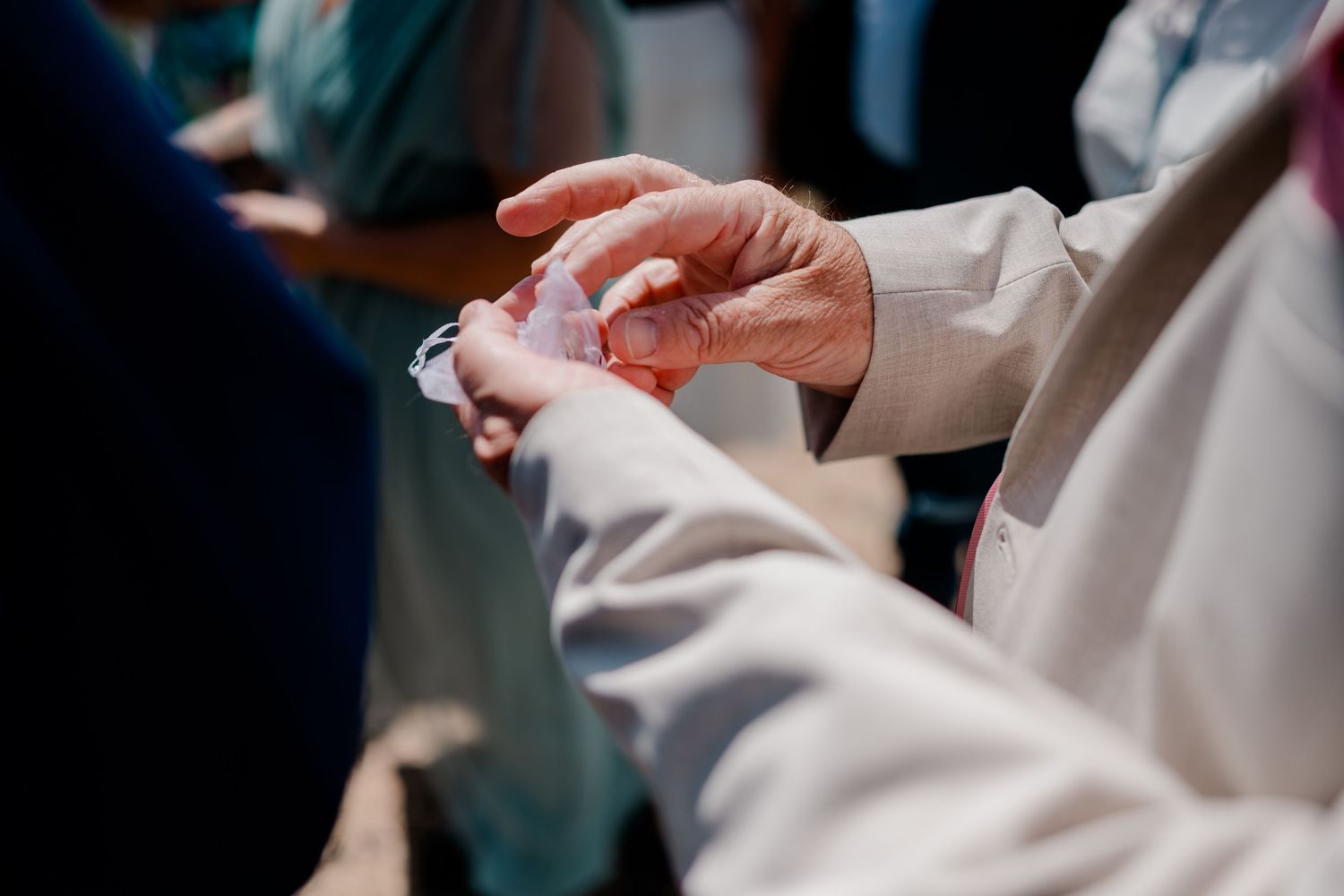 Close-up of hands exchanging wedding rings during an outdoor ceremony.