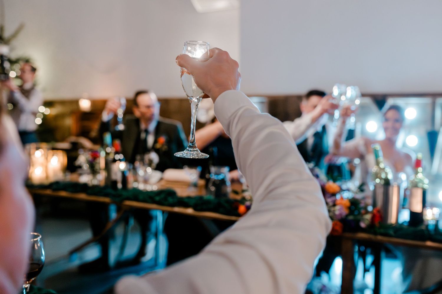 A guest raises a champagne glass in a toast at an elegant wedding reception dinner.