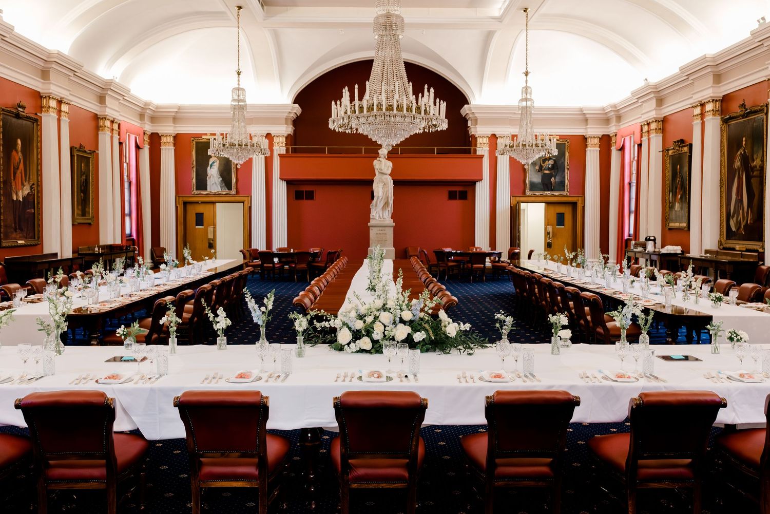 A panoramic view of an elegant ballroom with chandeliers, red walls, and formal dining tables set for a grand event.