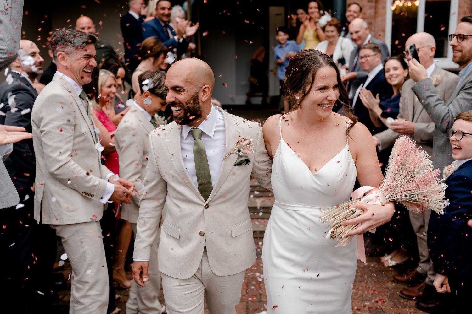 Wedding guests celebrate and throw confetti at a lively indoor reception.