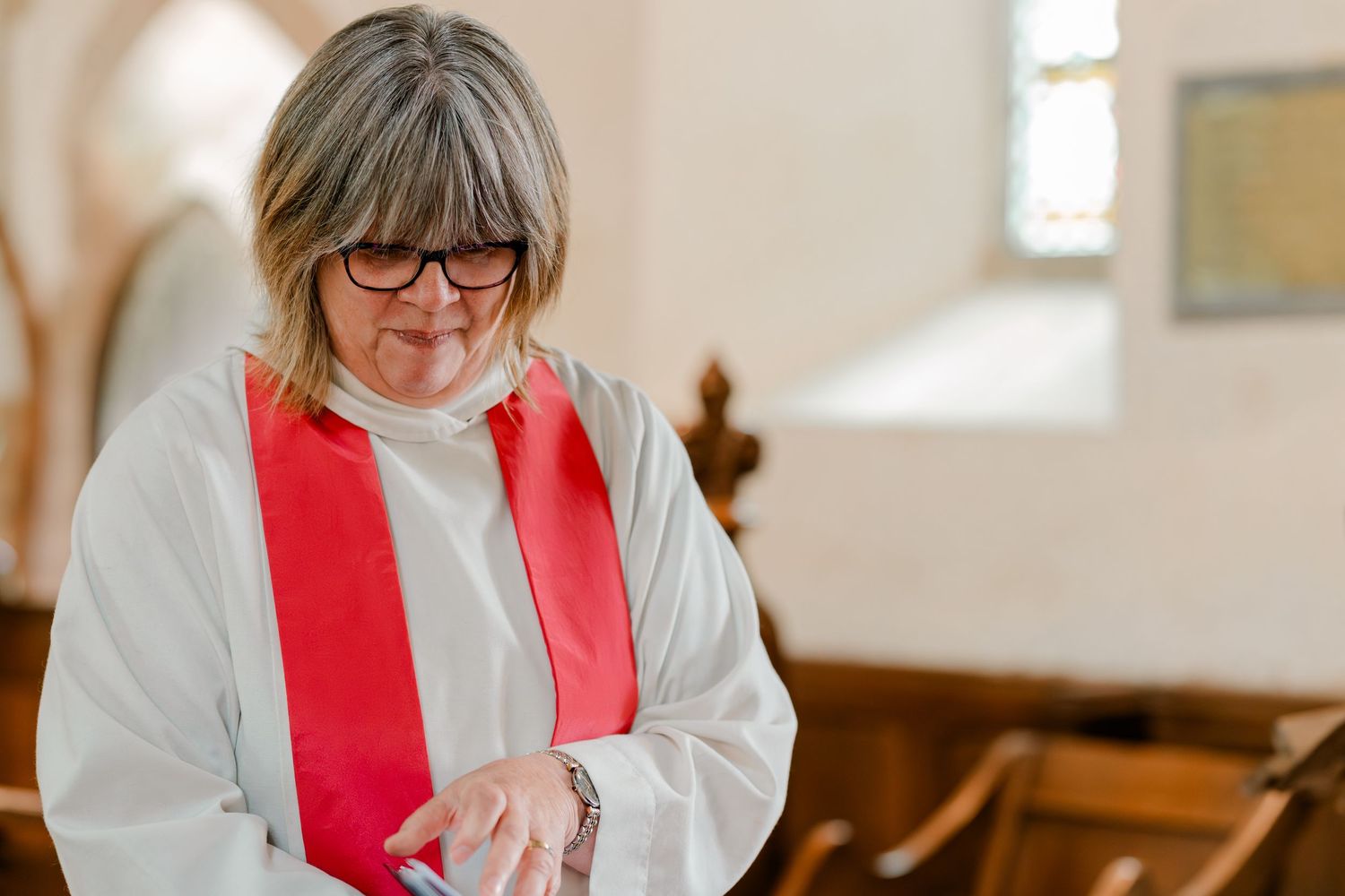 Female vicar in white robes with red stole officiating a church wedding ceremony.