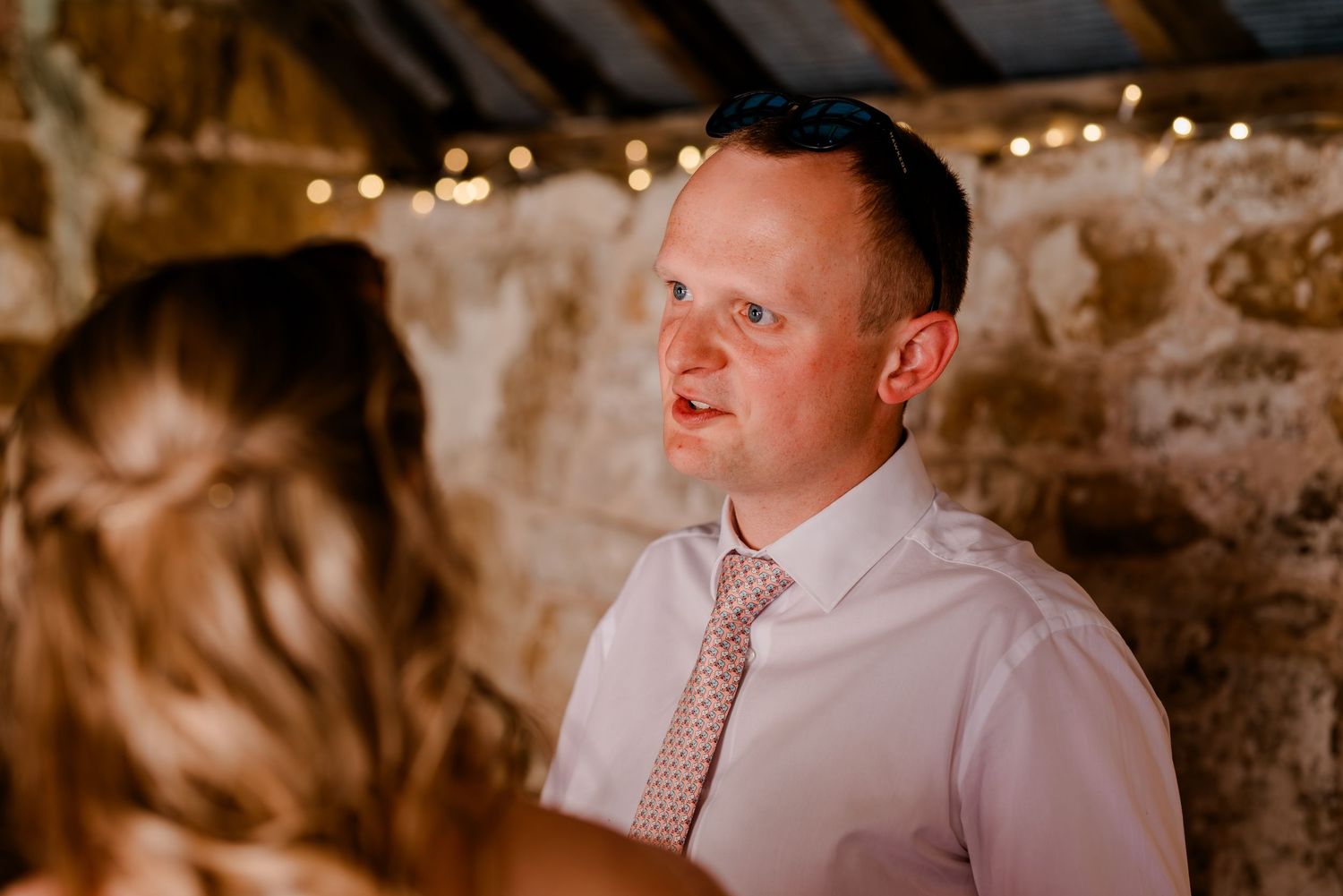 Wedding guests gather in a charming rustic stone venue decorated with warm string lights for an indoor celebration.