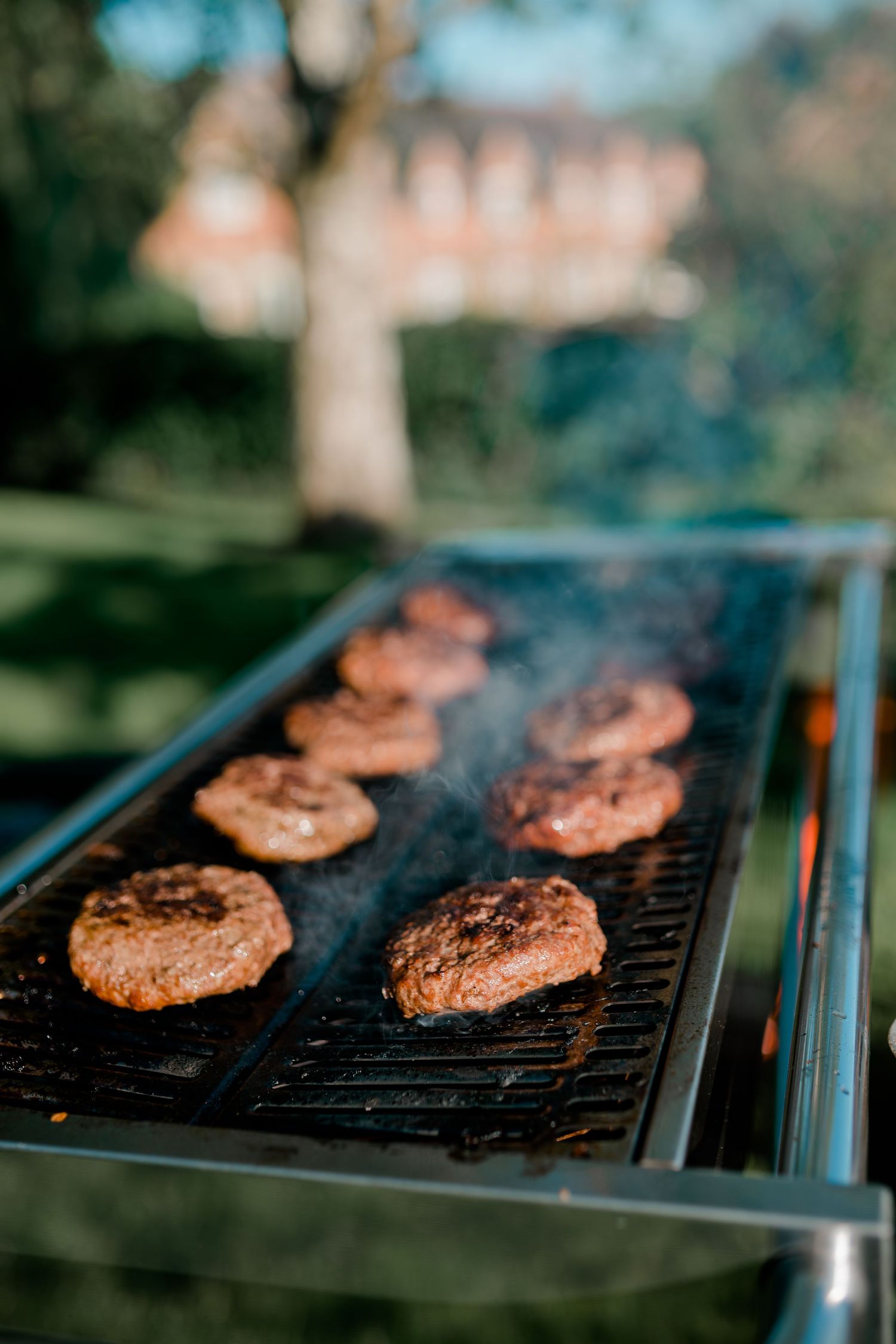 Hamburger patties cooking on outdoor grill with smoke rising.
