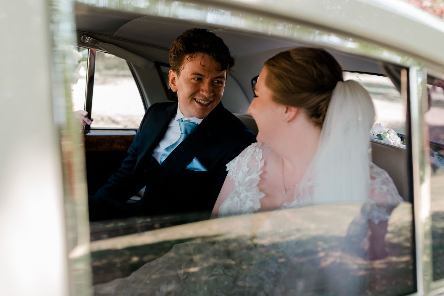 Wedding guests smile and laugh inside a classic car during a joyous celebration.