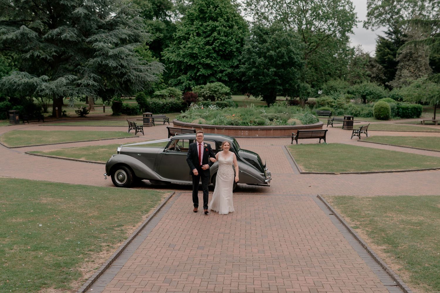 Classic cars parked along a brick-paved pathway in a garden setting.