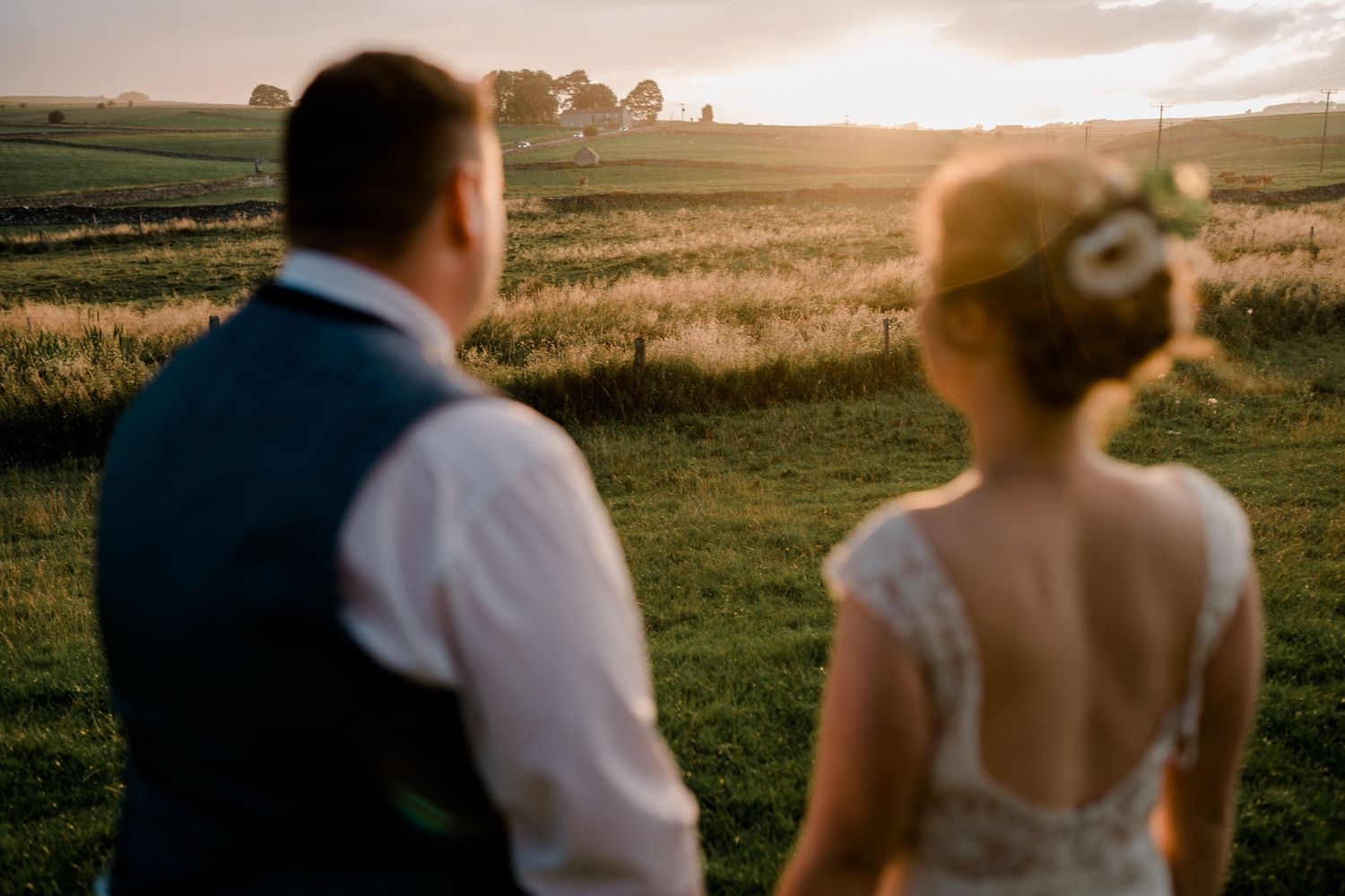 Bride and groom admire a stunning golden sunset over open fields during their outdoor wedding portraits.