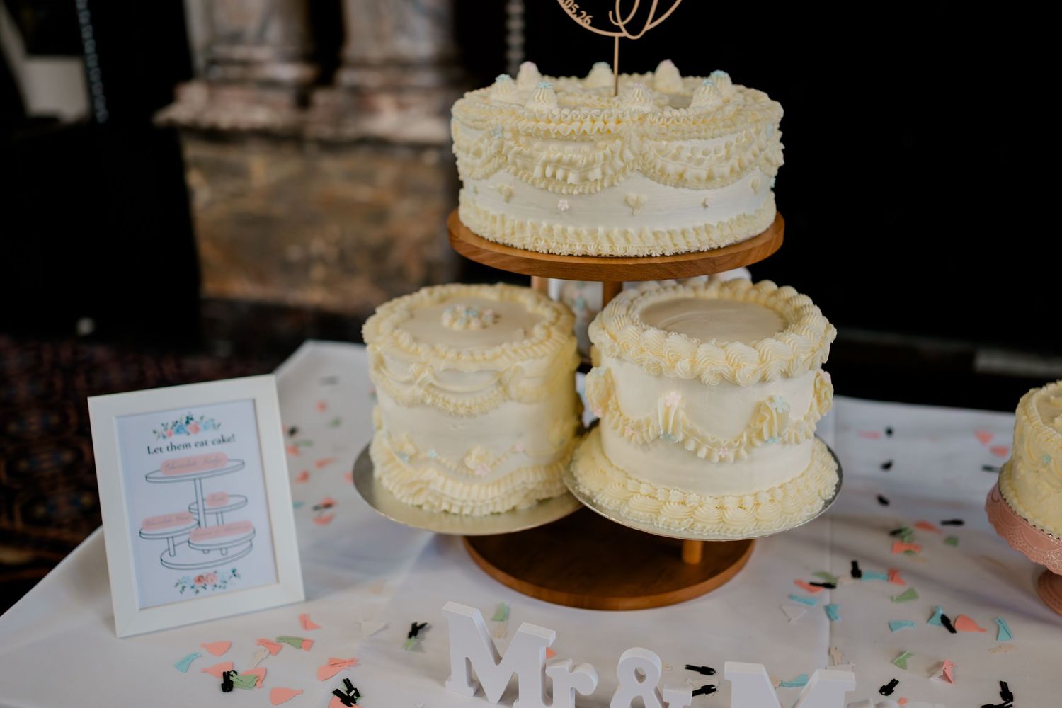 Elegant three-tier white wedding cake with pearl decorations displayed on a gold stand beside a Mr. & Mrs. sign.
