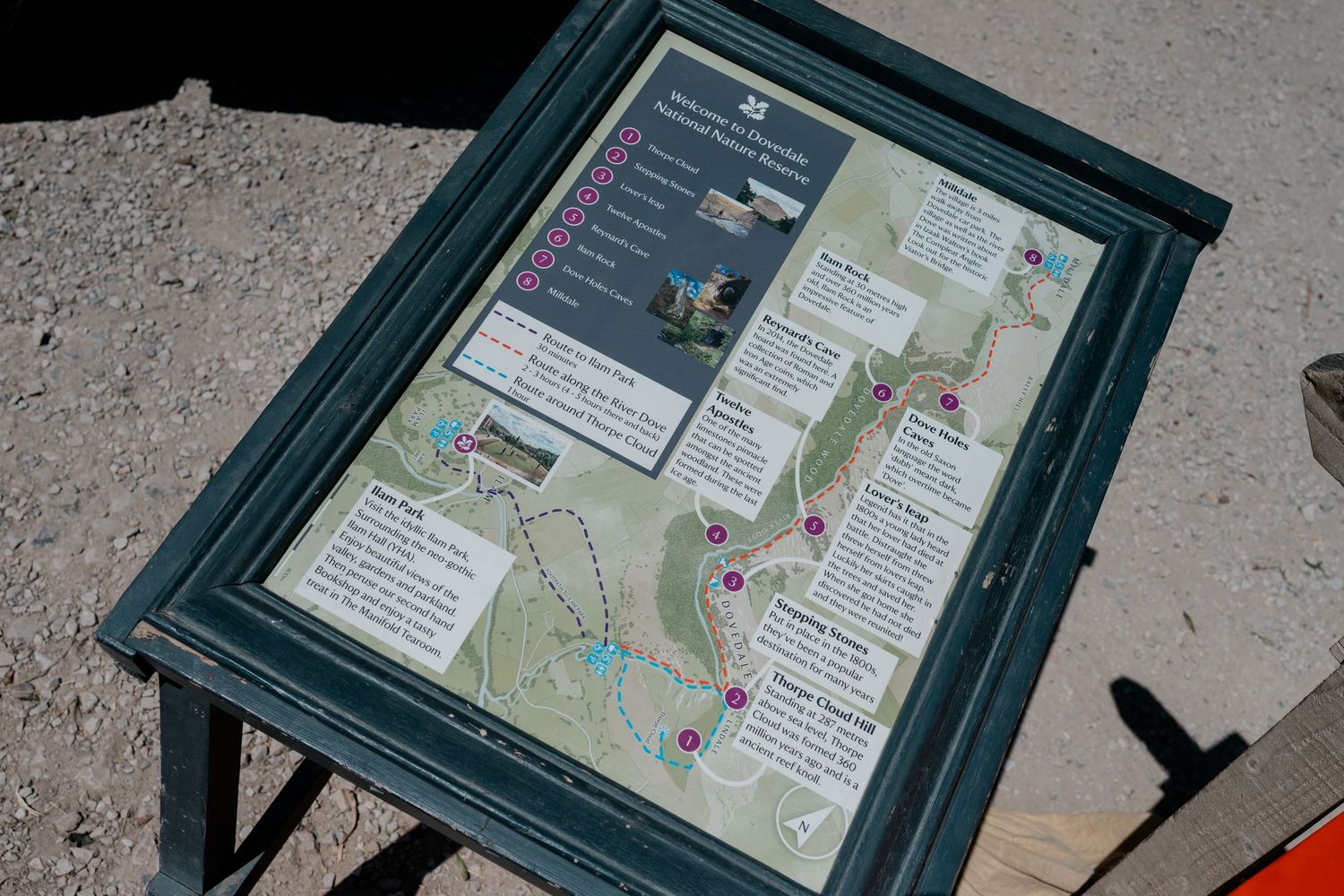Outdoor trail map sign in green frame mounted on stand showing park paths and points of interest.