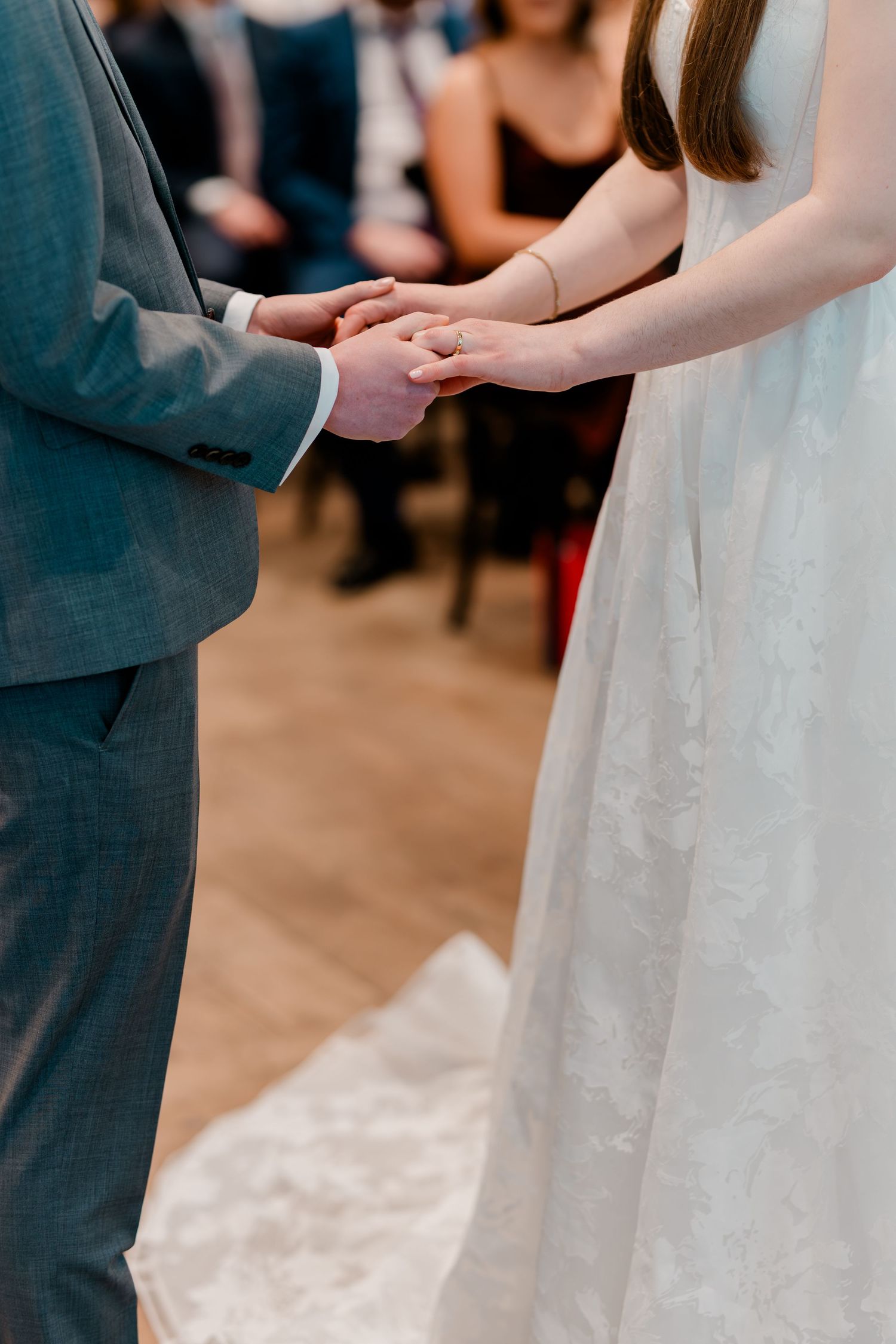 Bride and groom exchanging rings during wedding ceremony, close-up of hands holding together in elegant attire.