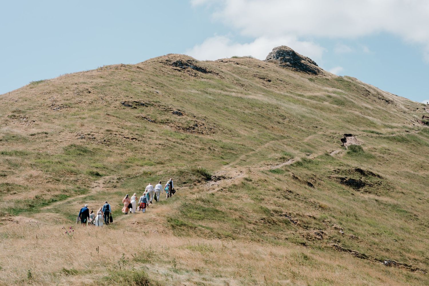 Group of wedding guests climbing a winding path up a green hillside.