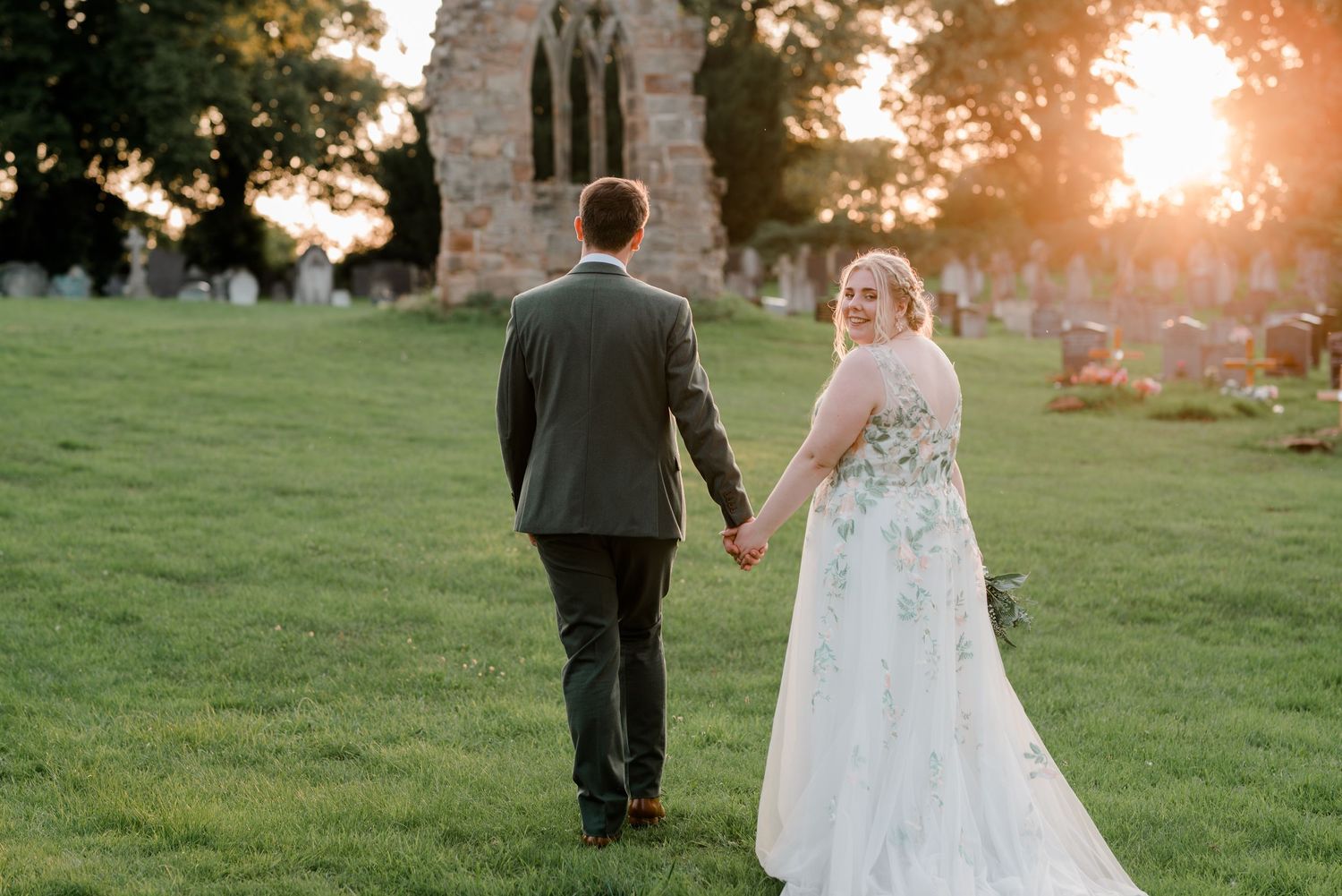 Couple walking through grassy field during golden hour sunset.