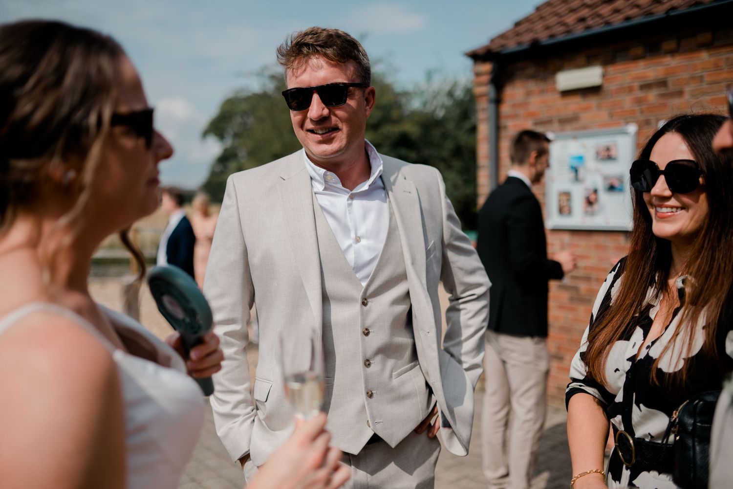 Wedding guests socialize outdoors on a sunny summer afternoon.