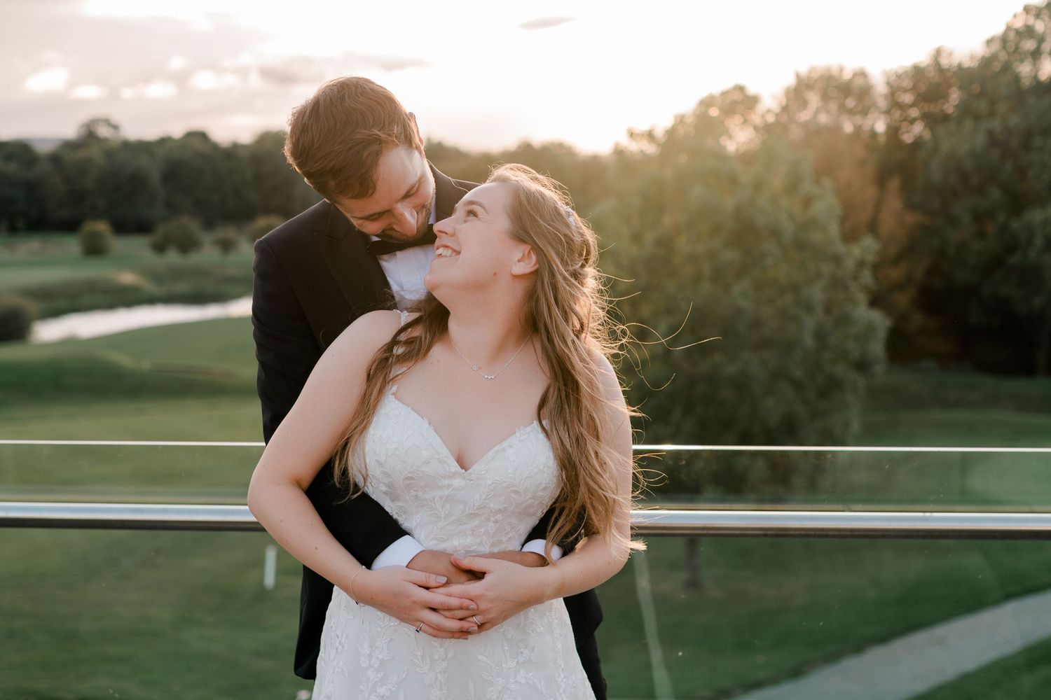 Bride and groom embrace tenderly at golden sunset during outdoor wedding portrait at a golf course venue.