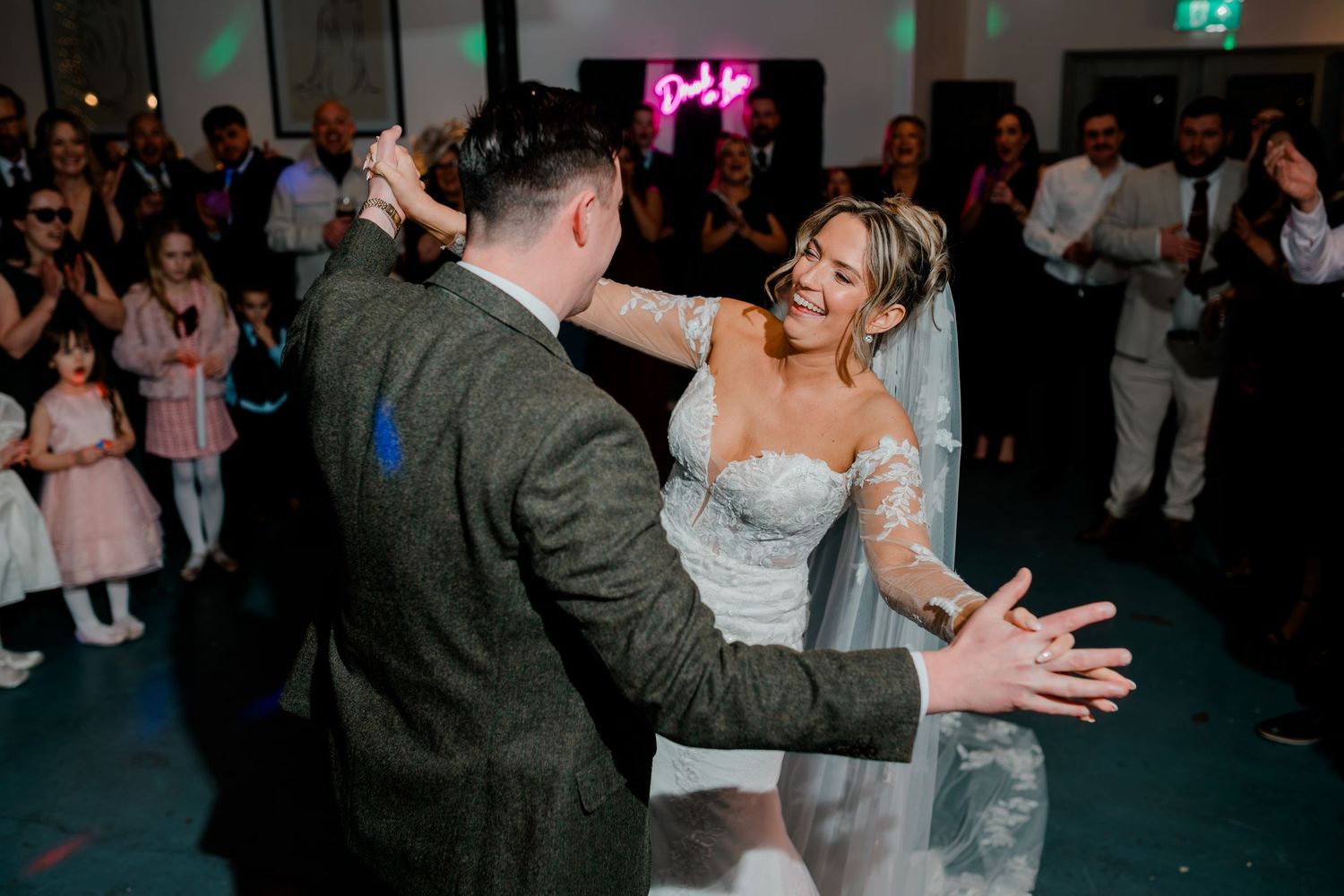 Bride in lace wedding dress laughs joyfully with groom during energetic first dance at wedding reception.