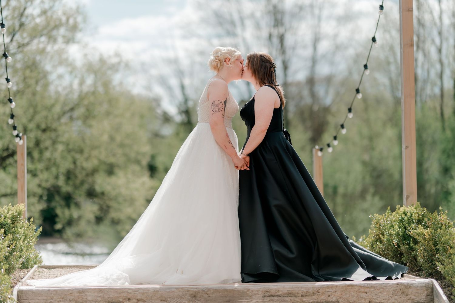 Two brides share a kiss at their wedding ceremony, one in white gown and one in black dress.