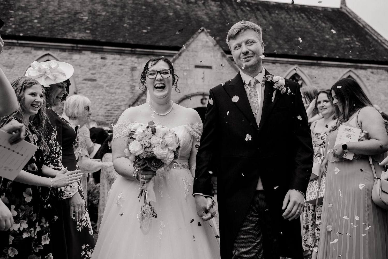 Bride and groom walking through confetti after their wedding ceremony outside a stone church.