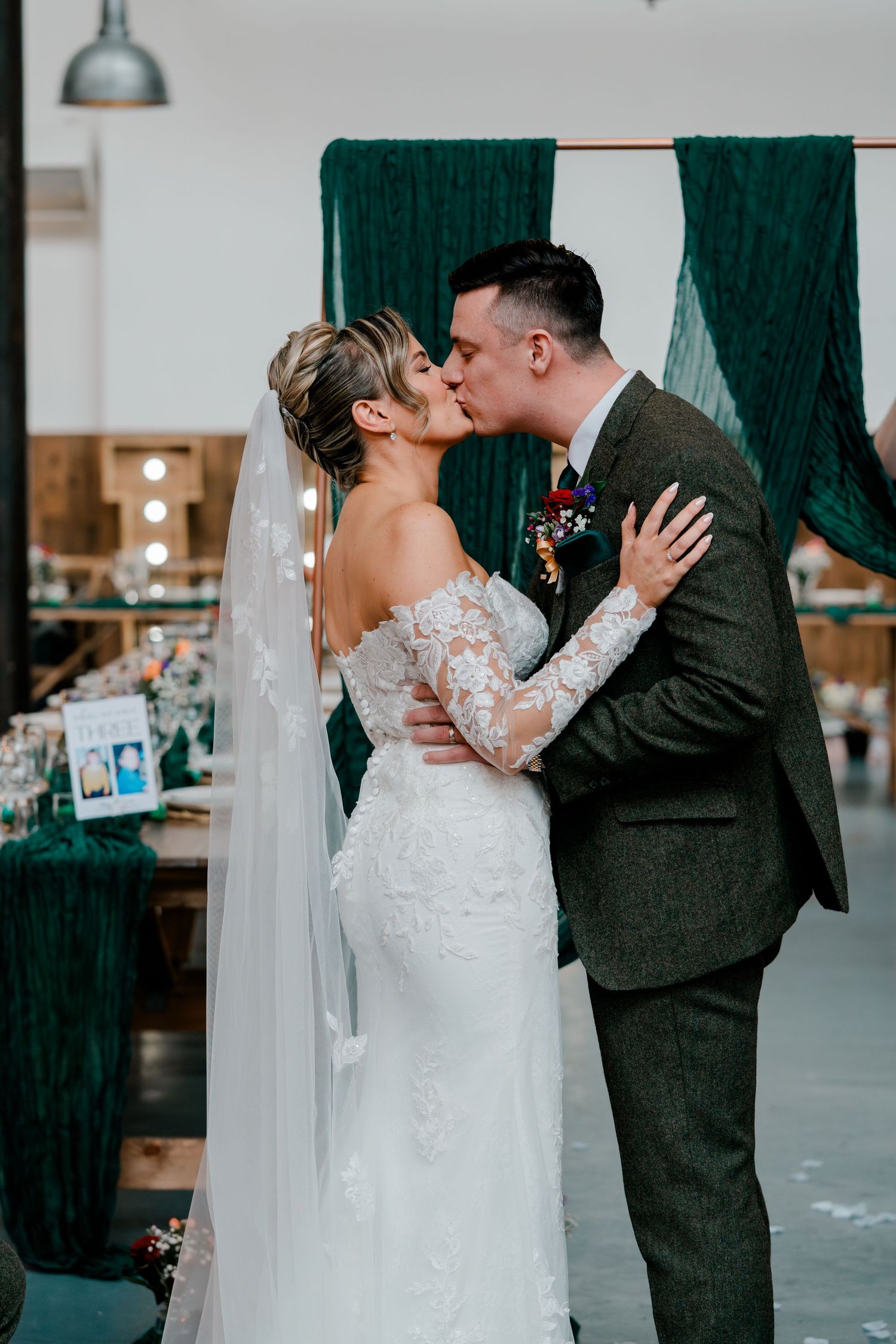 Bride and groom share their first kiss at wedding ceremony with green velvet drape backdrop decoration.
