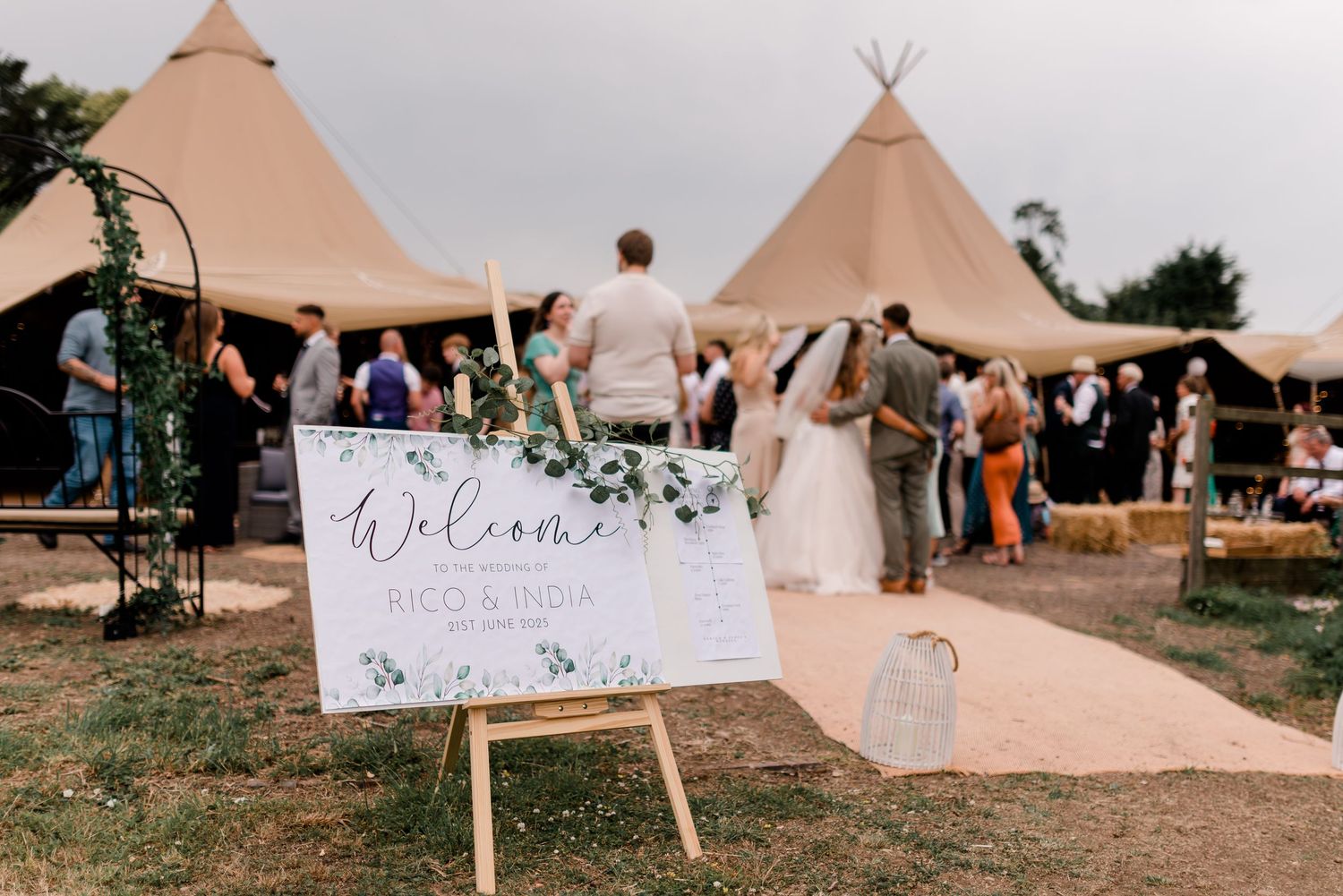 Row of boho-style tipi tents set up for an outdoor wedding celebration against a sunset sky.