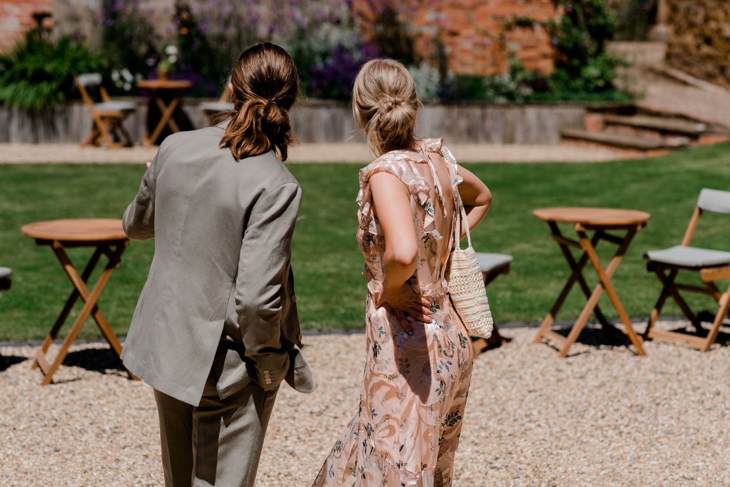Wedding party walking outdoors on gravel path with wooden folding chairs in background.