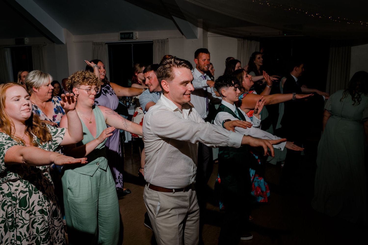 Wedding reception guests dancing together in a dimly lit venue.