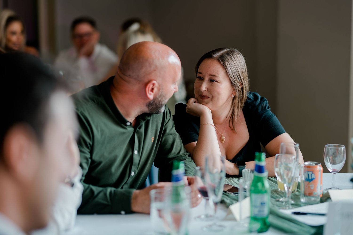 Guests enjoying conversation at a dinner table with water bottles and glassware.