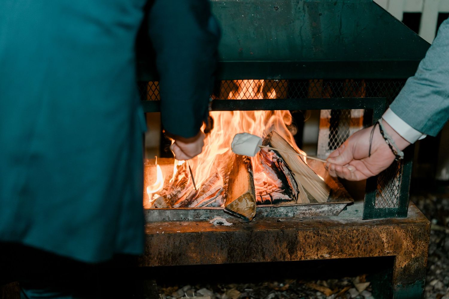 Couple roasting marshmallows over an outdoor fire pit at a wedding celebration.