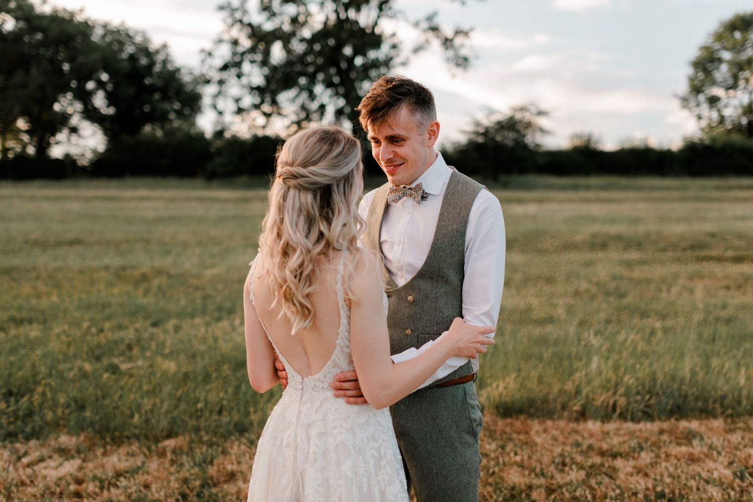 Newlyweds embrace in a sun-drenched field during golden hour.