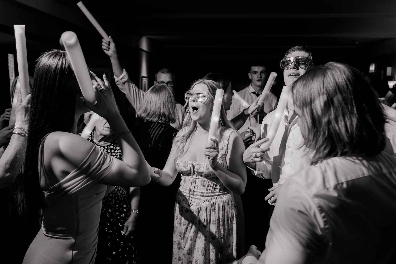 Wedding guests enjoying themselves and dancing together on a dark dance floor at an evening reception celebration.