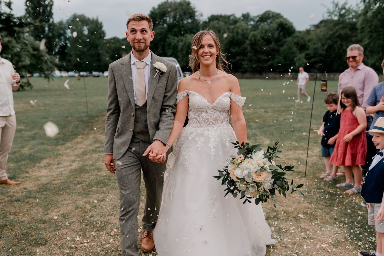 A newlywed couple walks across a grassy field during their outdoor wedding celebration.