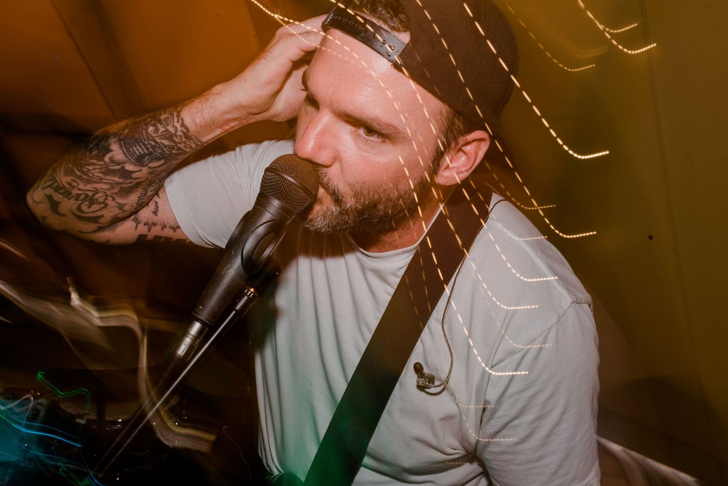 Musician with tattoos and beard sings passionately into microphone during nighttime performance.