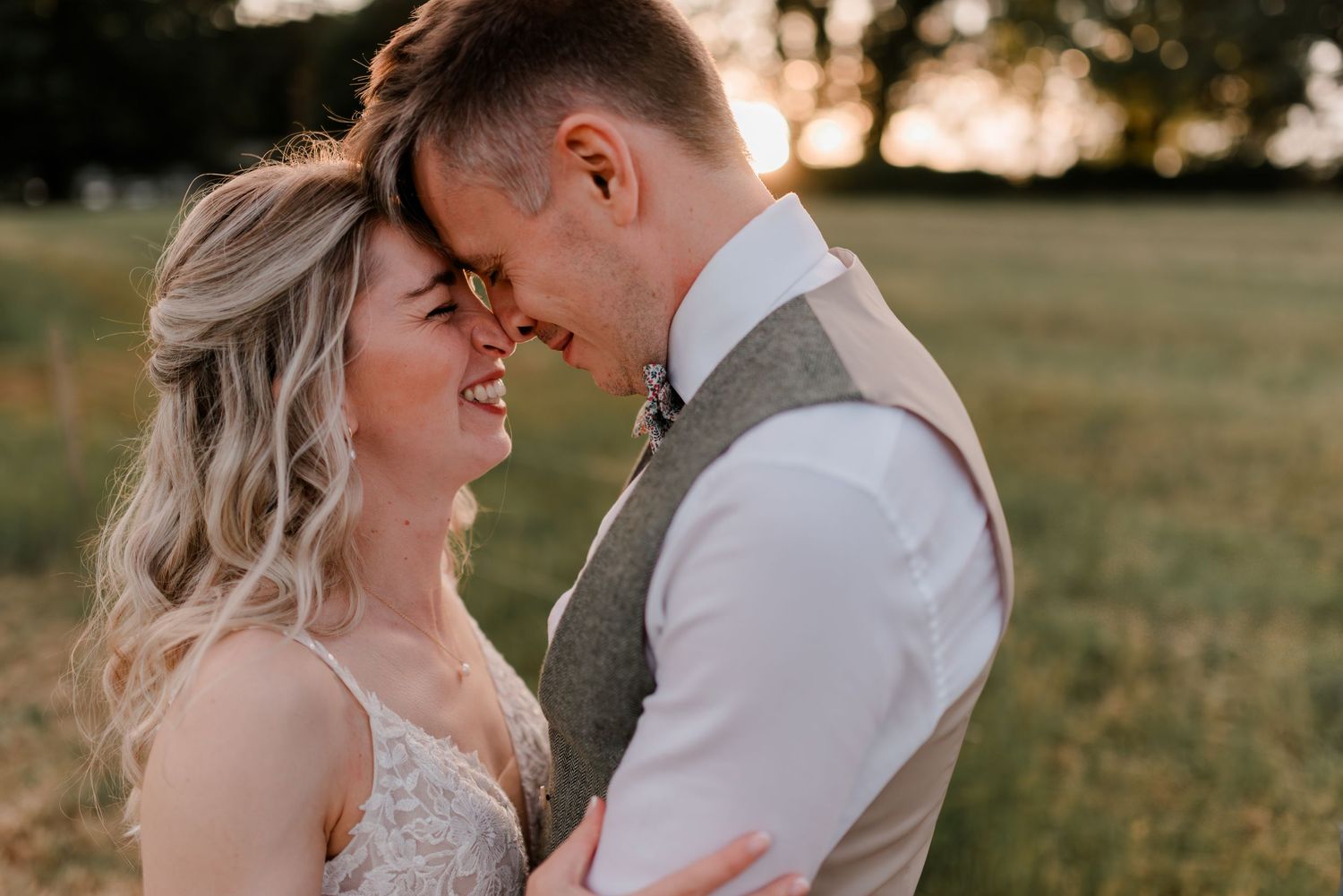 Happy bride and groom share a romantic close moment at golden hour in an open field.