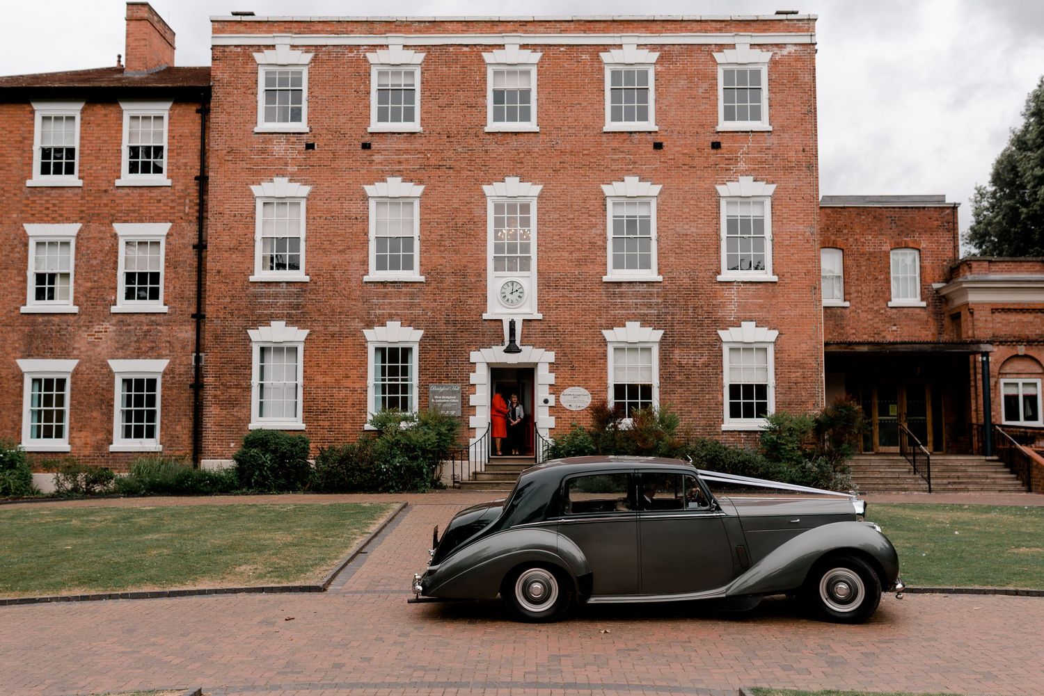 Vintage classic car parked outside a grand red brick Georgian building on a wedding day.