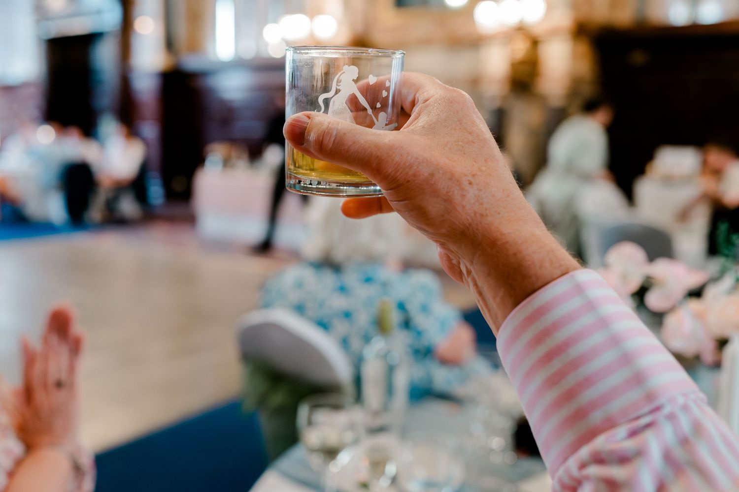 Guest raises a glass of whiskey for a toast at an elegant wedding reception celebration.