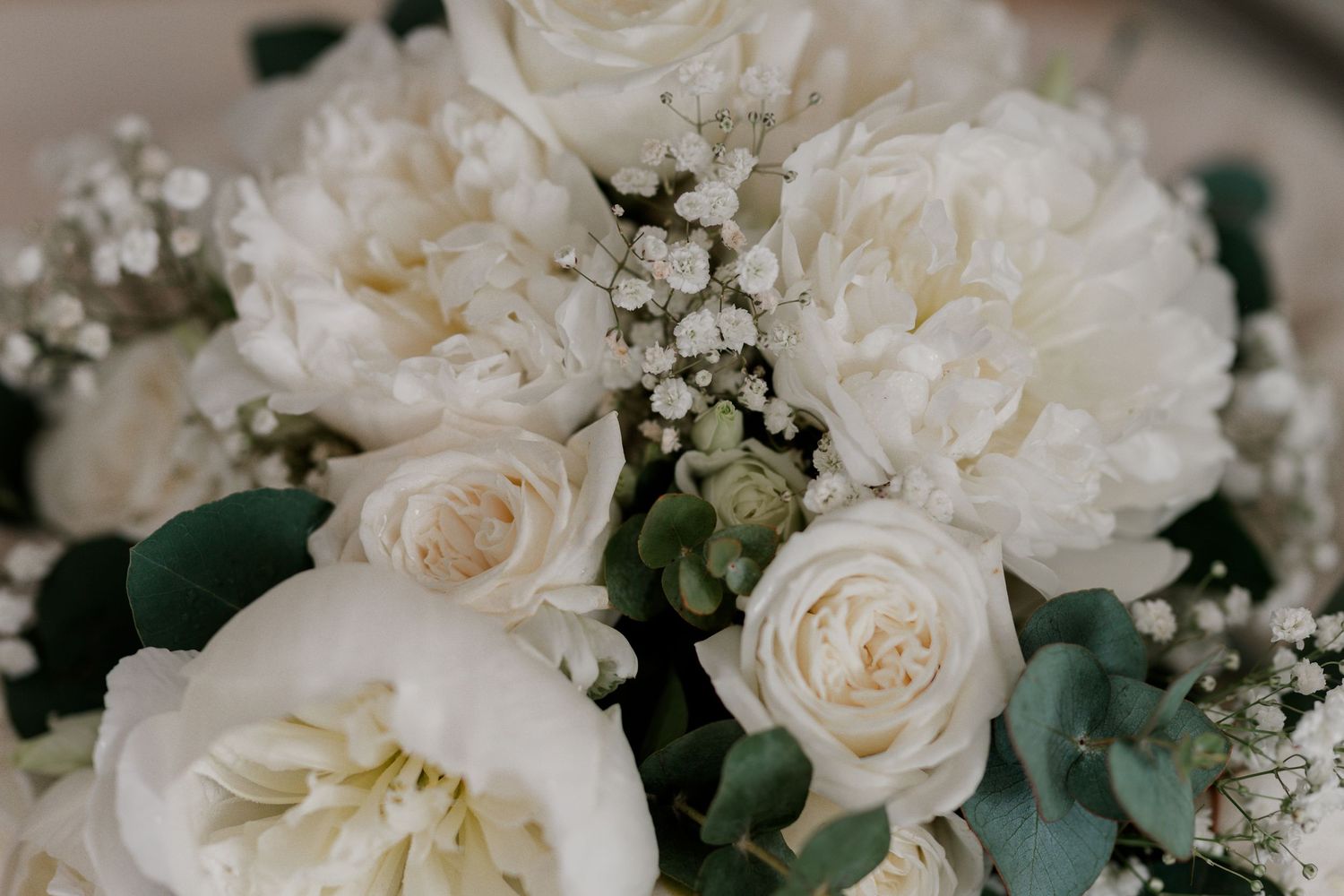 Elegant white wedding bouquet with peonies, roses, baby's breath, and eucalyptus leaves.