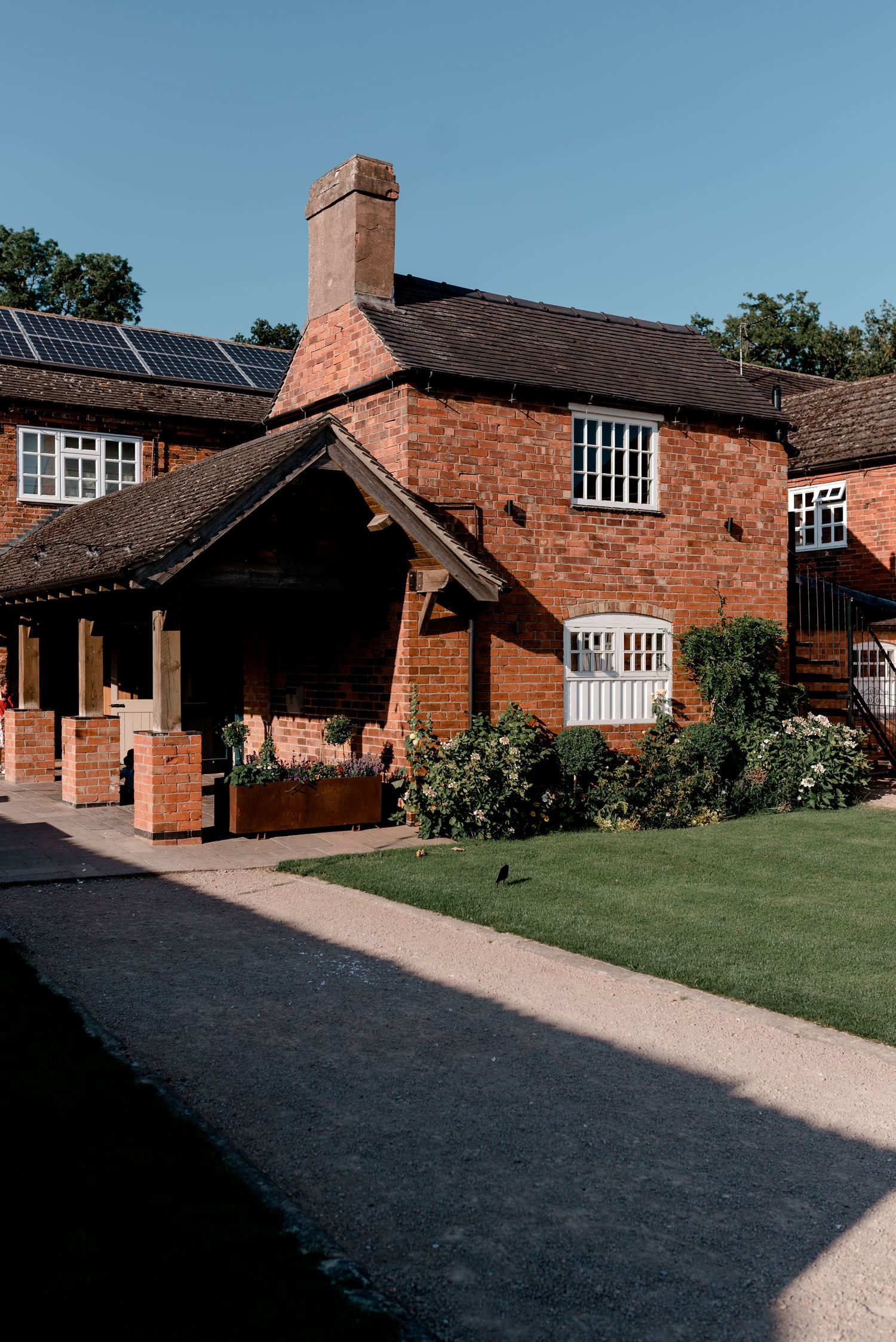 Red brick farmhouse venue with manicured lawn and gravel pathways on a sunny day.