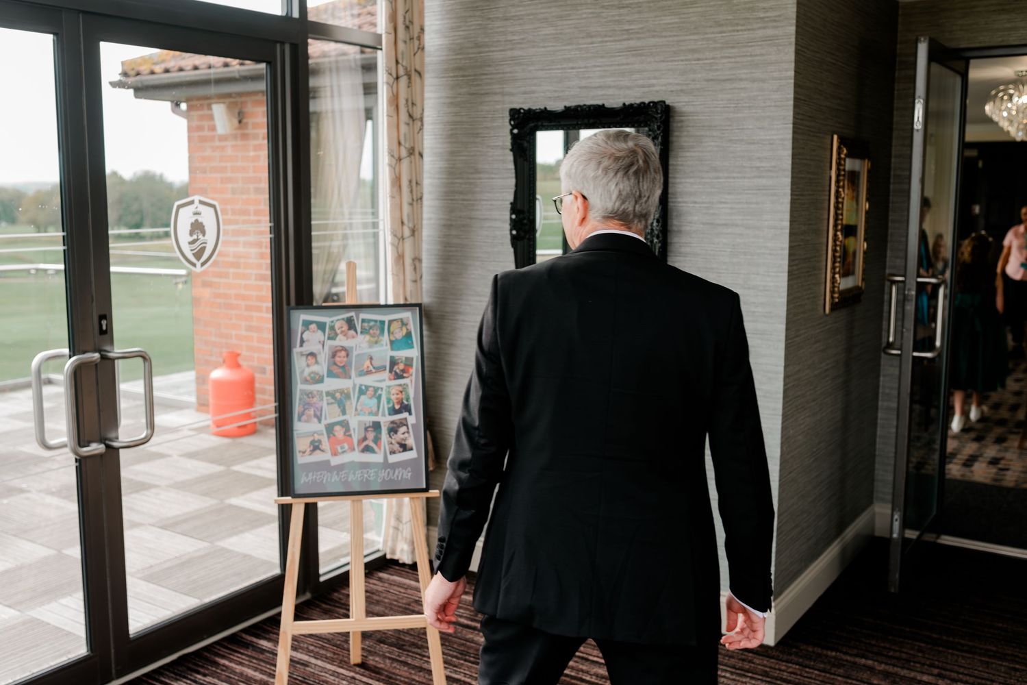 People in business attire walk through a covered passageway with brick walls and glass windows.