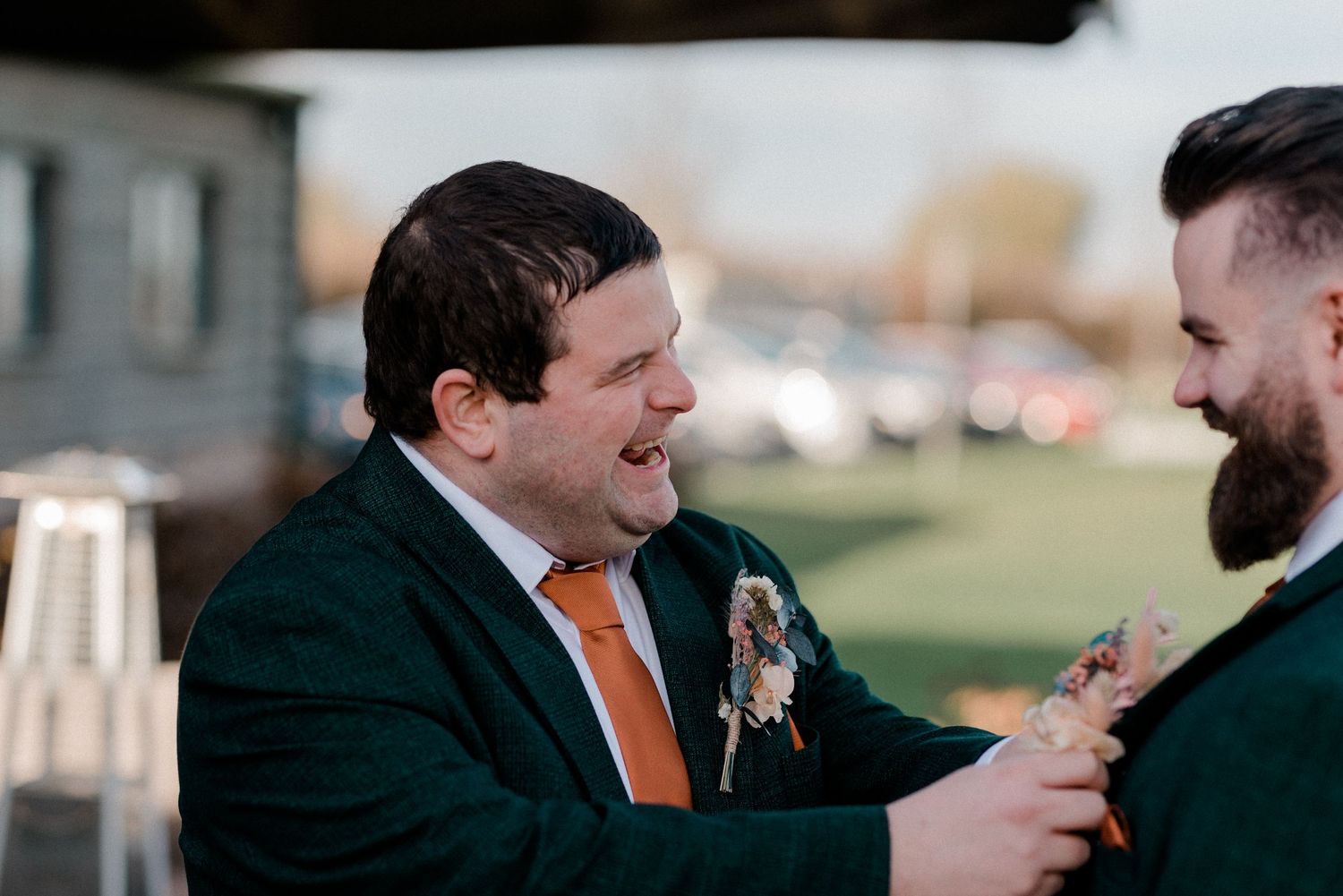 Two people share a candid laughing moment outdoors during a wedding celebration at sunset.
