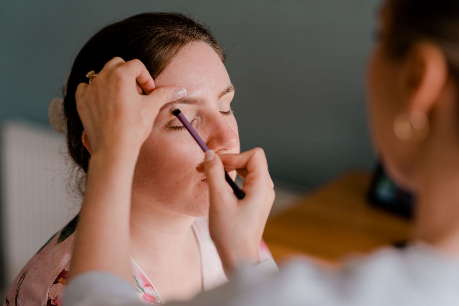 A makeup artist carefully applies eye makeup on someone during wedding preparations.