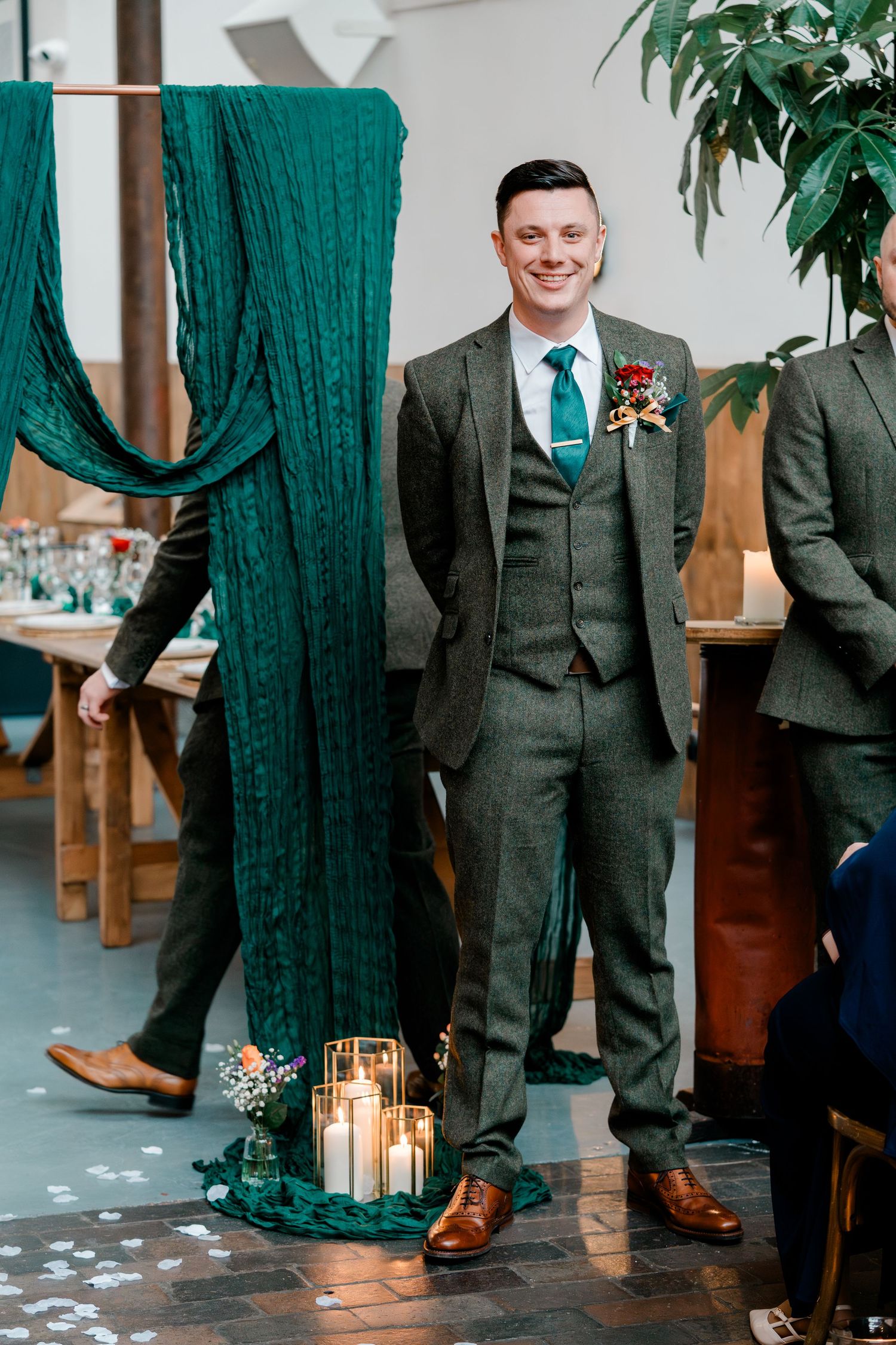Smiling groom in green tweed three-piece suit at wedding ceremony altar.