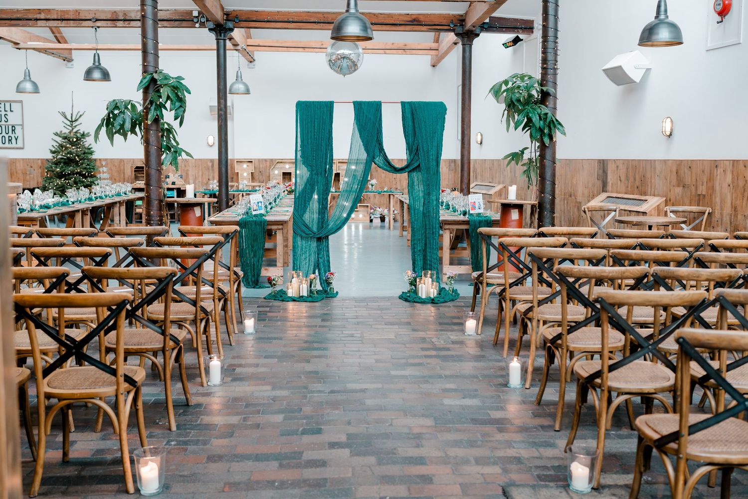 Wedding ceremony venue with teal drape arch, wooden chairs, and candles.
