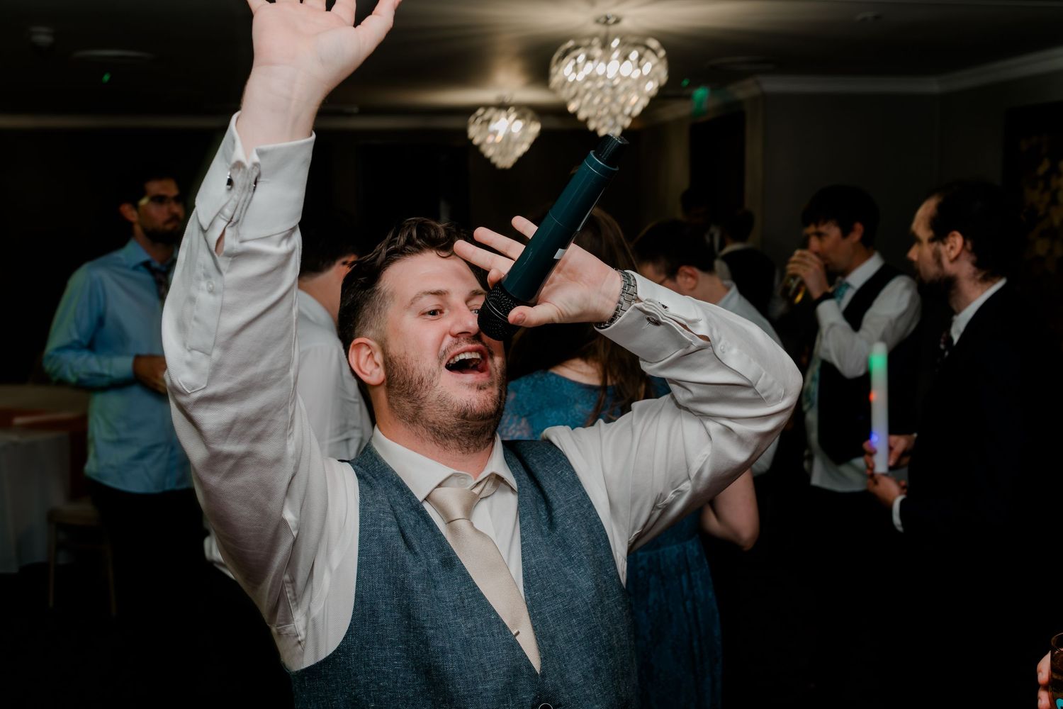 Guests raise their hands in celebration during an energetic dance party at a wedding reception.