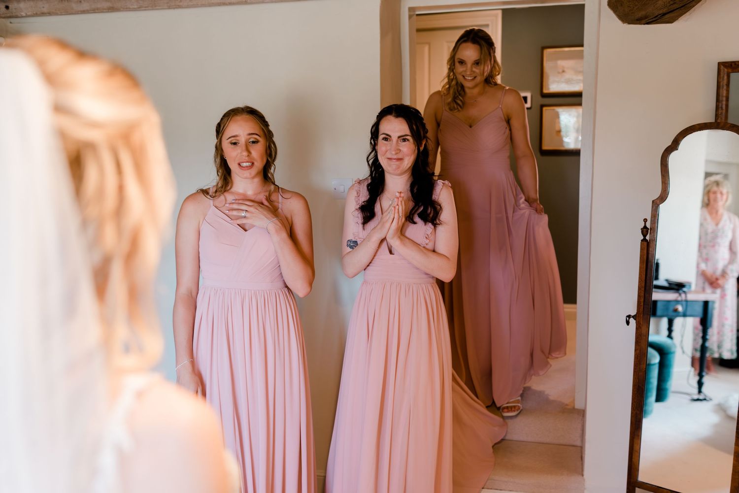 Bridesmaids in light pink flowing dresses stand together in a bright indoor space for wedding photos.